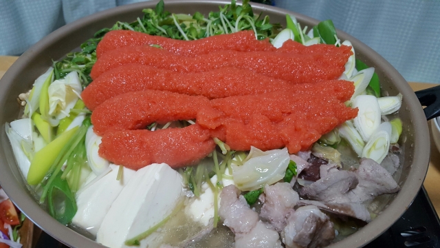 Close up of five pieces of mentaiko on top of a large hot pot with tofu, vegetable and seafood.