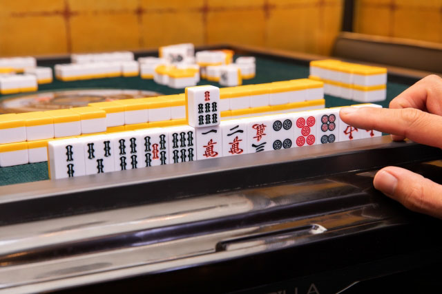 Close up of mahjong pieces lined up on a Mahjong table with a person's hand near.