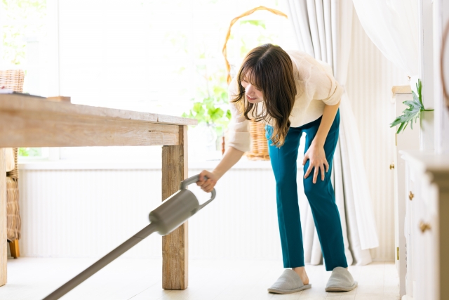 Female person using the vacuum cleaner to clean underneath the table