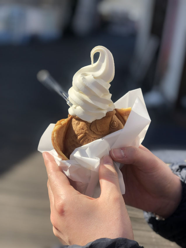 A woman's hand holding a taiyaki with soft ice cream on top