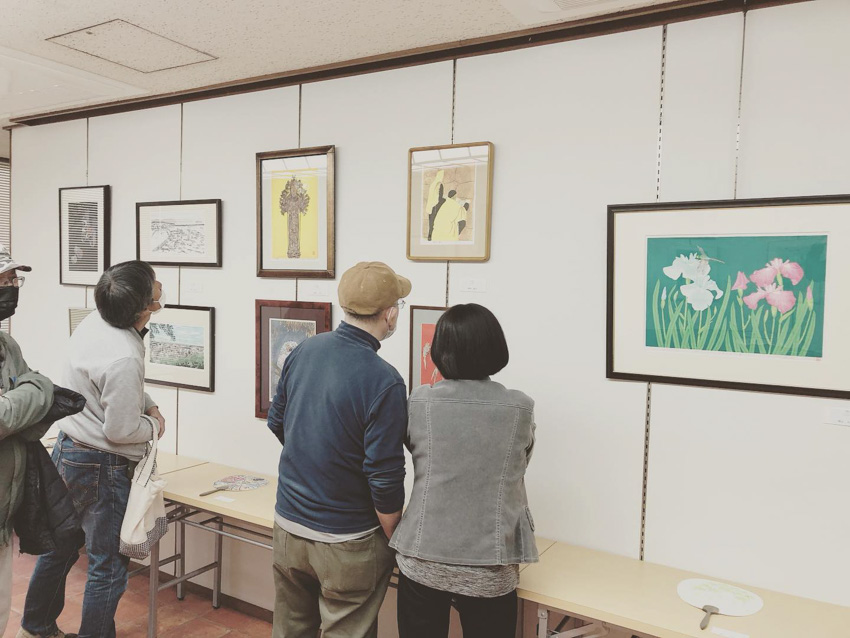 Three people viewing woodblock prints hanging on a wall