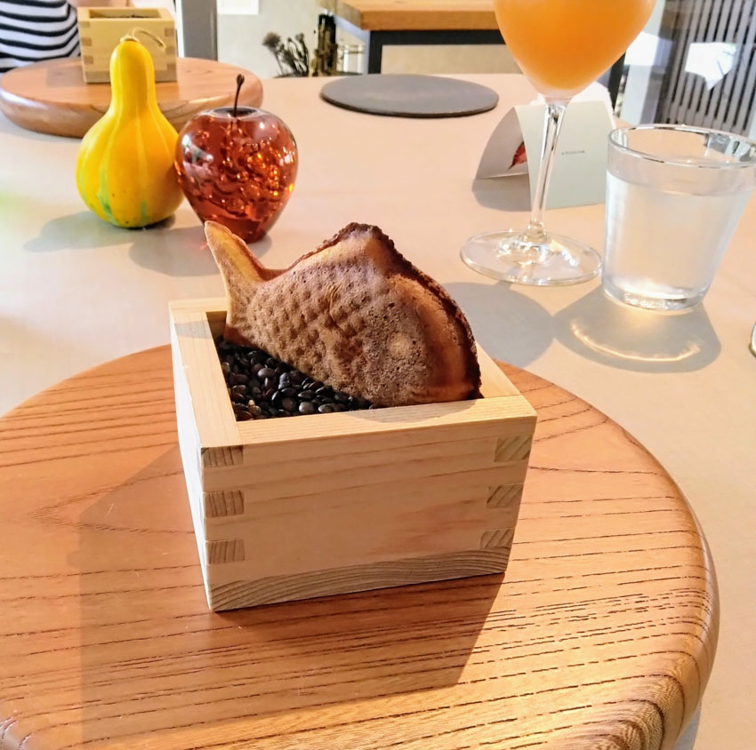 Taiyaki placed in a wooden sake cup filled with coffee beans on a table