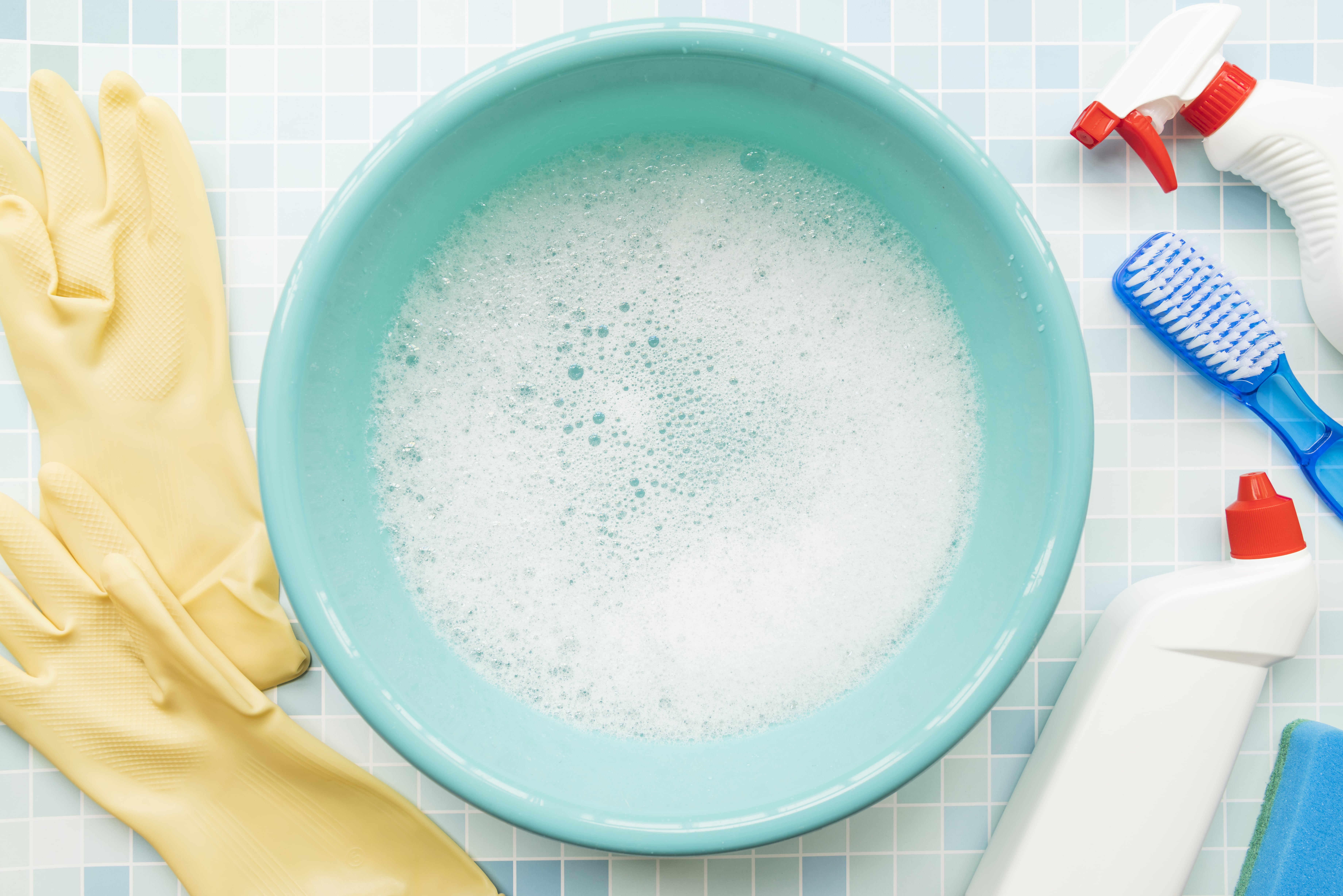 Turquoise blue pail with soapy water inside and cleaning tools around on a tiled floor