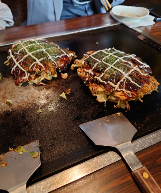 Two Japanese pancakes called Okonomiyaki on top of a hot plate