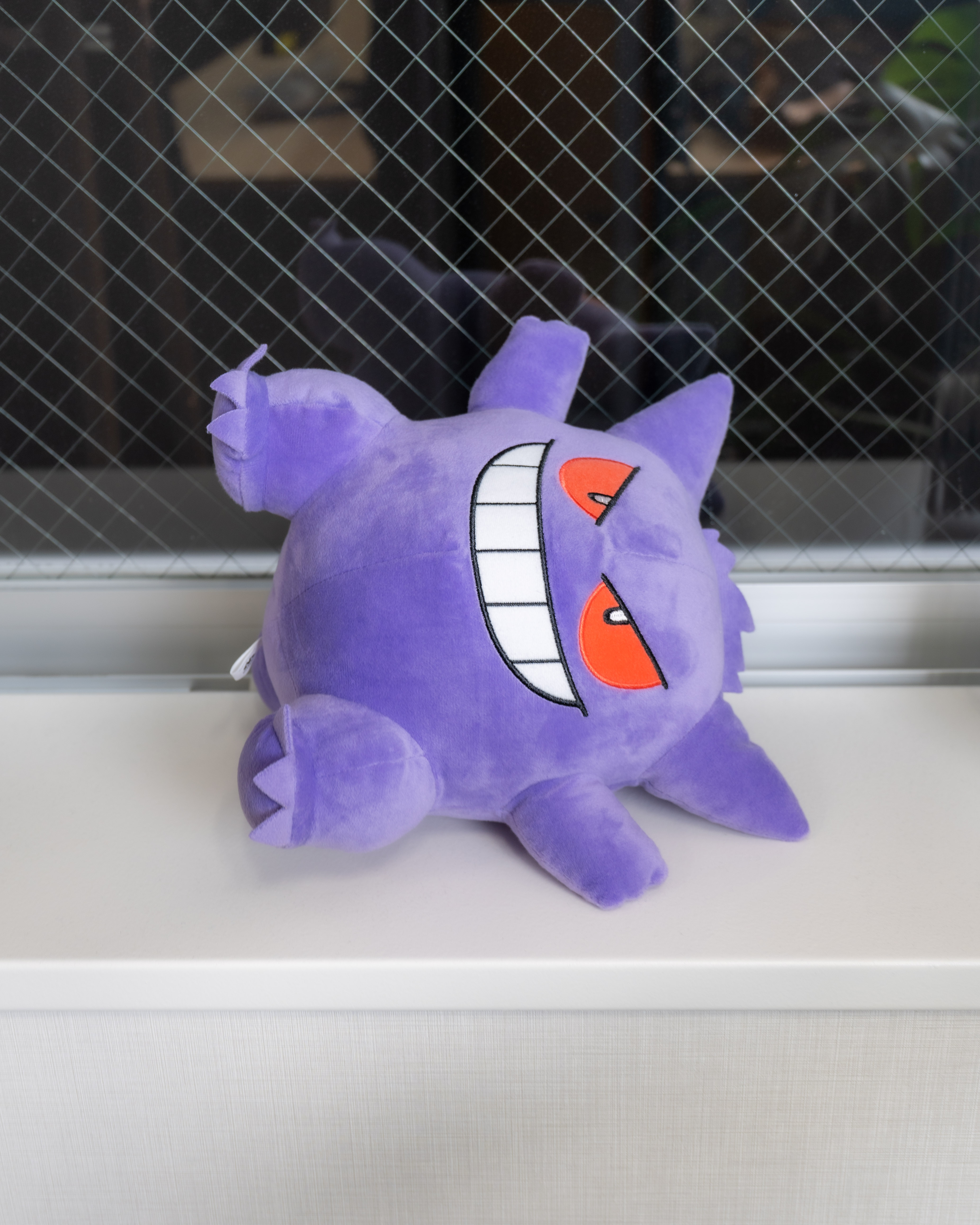 Purple Gengar plushie laying sideways on white windowsill