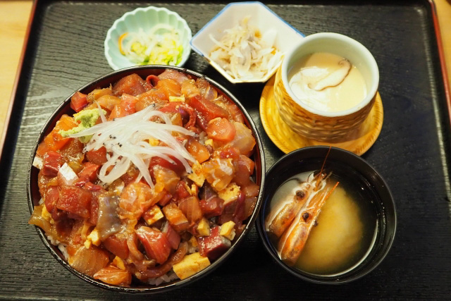 A set meal with donburi as the main dish surrounded by soups and salad on a black tray