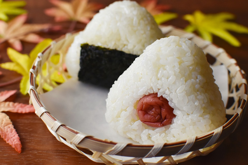 Two onigiri in a wooden basket type bowl.