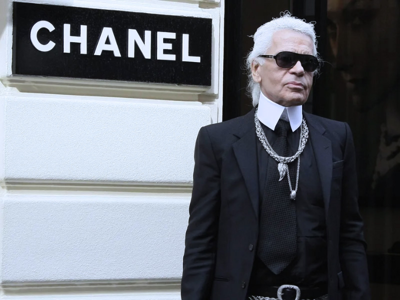 Carl Lagerfeldt infront of a Chanel sign