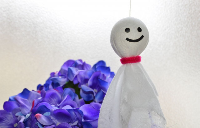 A smiling Teru Teru Bozu hanging in front of a purple flower