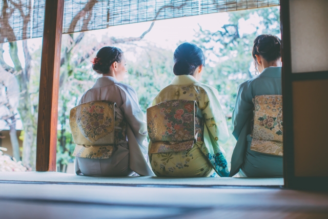 Three people wearing kimono, sitting facing the garden of a traditional Japanese house