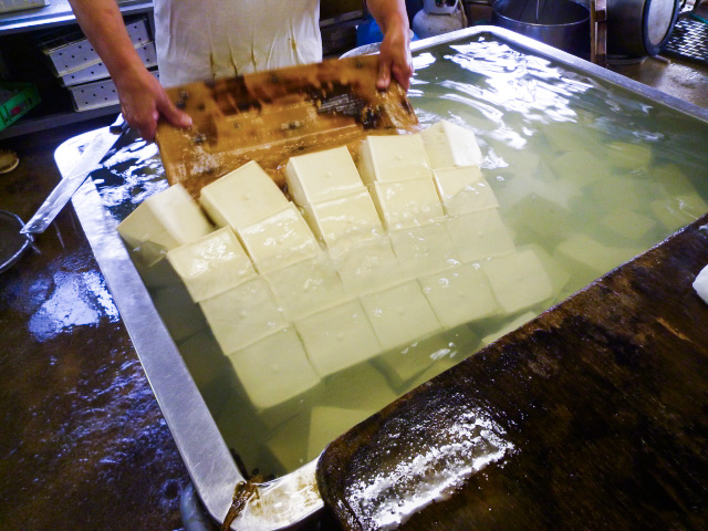 Tofu production - staff handling the cut tofu in a large tub filled with water.