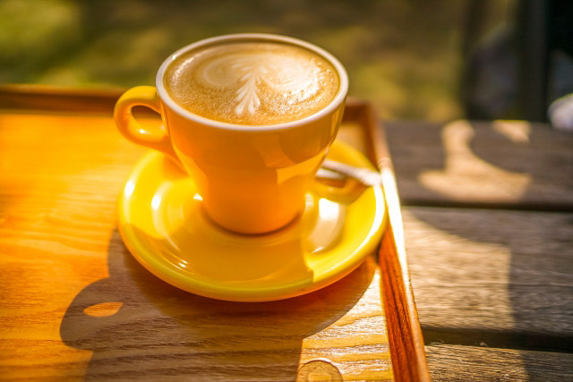 A cup of hot coffee on a wooden table in early morning sunlight