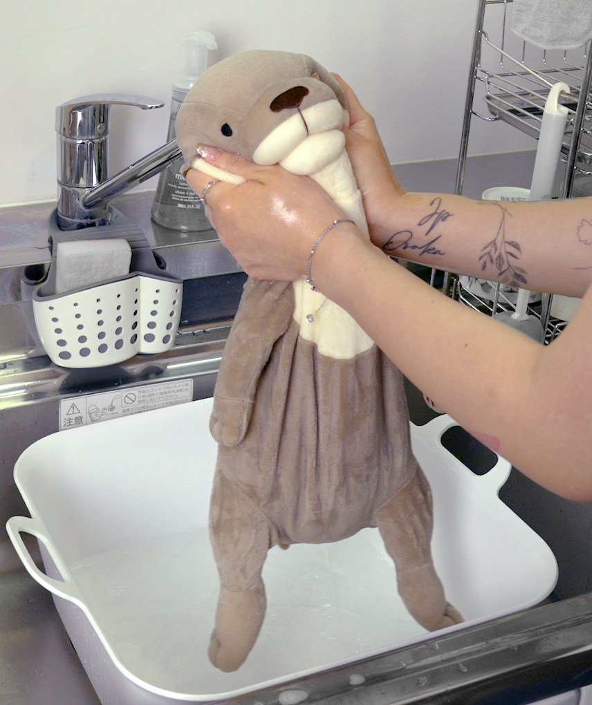 Person squeezing head of drenched stuffed gray otter 