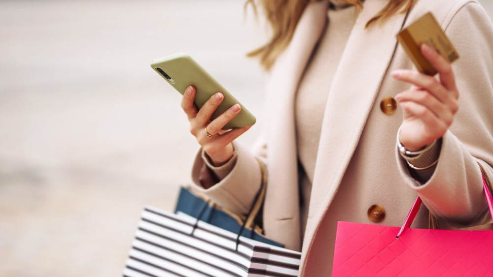 Woman holding a credit card and carrying several luxury shop bags. 