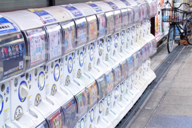 A long row of Gacha vending machines lined up on a street in Japan