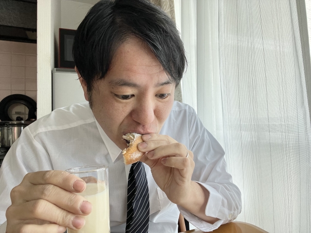 Male eating a piece of bread and holding a cup of milk with the opposite hand