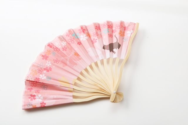 Close up of a pink fan with a cat and cherry blossom's print on it