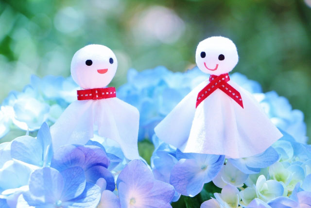 Two smiling Teru Teru Bozu dressed up to hint at a male and female sitting on blue flowers