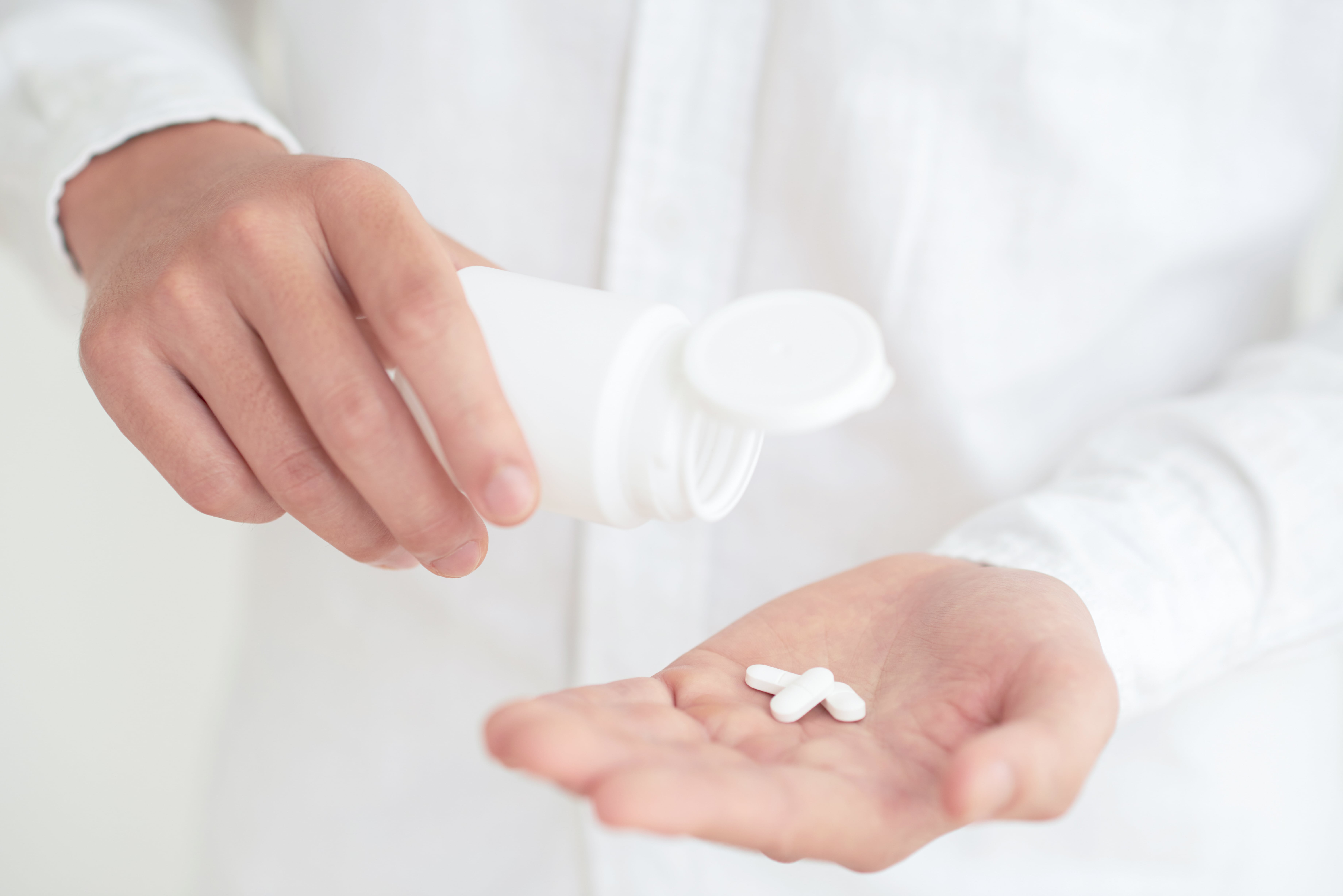 Person in white shirt putting 3 white tablets on left hand