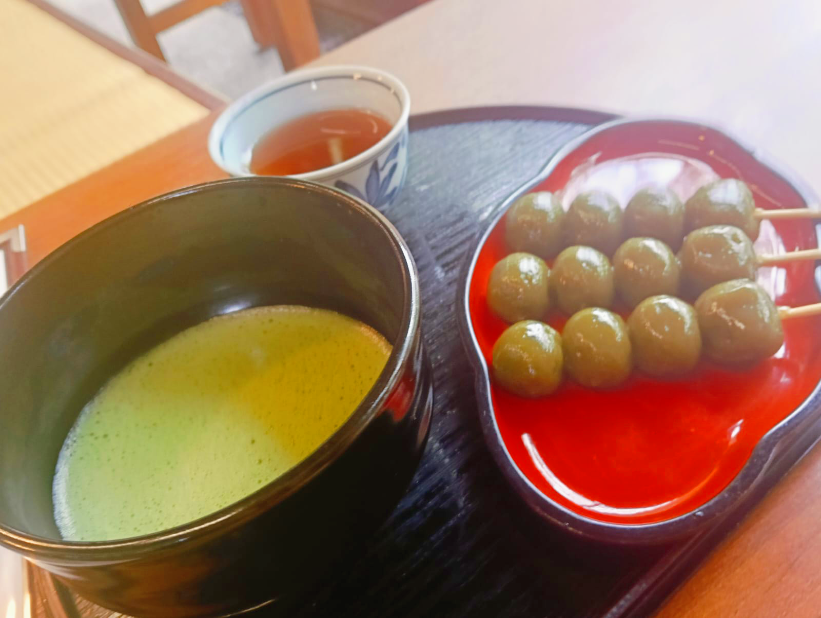 A traditional Japanese tea set featuring a bowl of matcha green tea, a cup of hot tea, and skewers of green tea–flavored dango