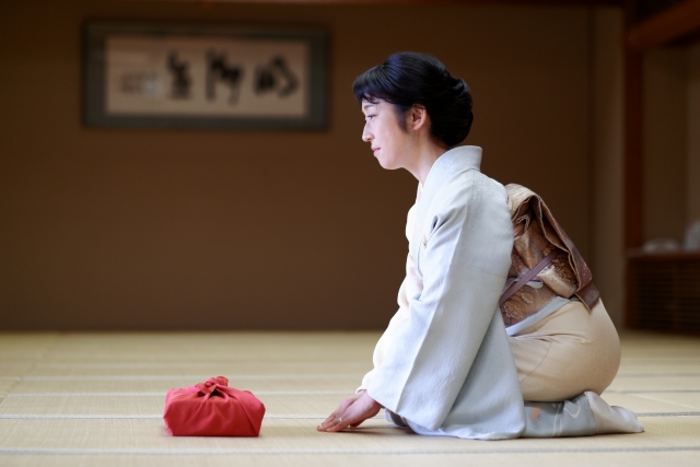 A female person wearing a traditional kimono sitting down on a tatami flooring
