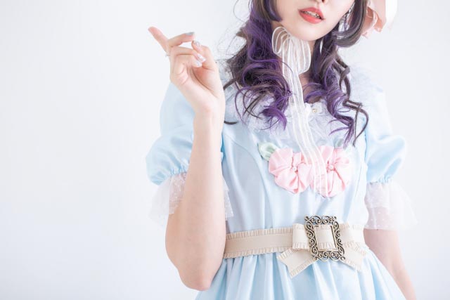 Close up of a girl wearing a light blue lolita fashion dress with pink accessories and white belt