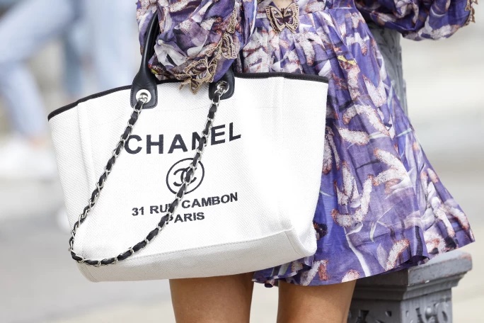 A person wearing a floaty lilac dress carrying a Chanel Deauville bag