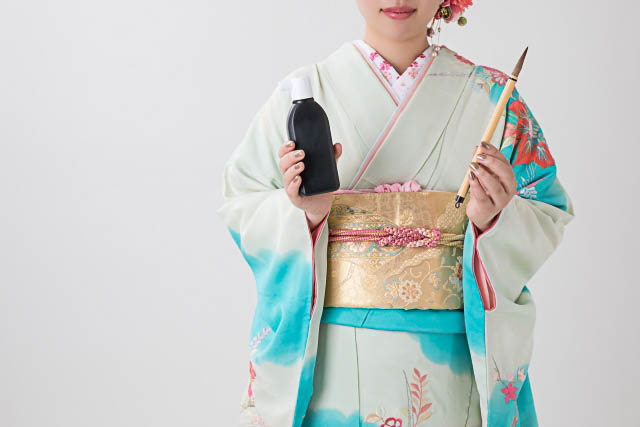 A woman dressed in kimono holding a calligraphy brush and a bottle of ink,