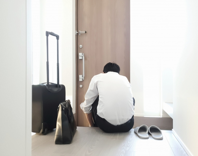 A person sitting at the entrance of a Japanese house with a handbag and a luggage near them