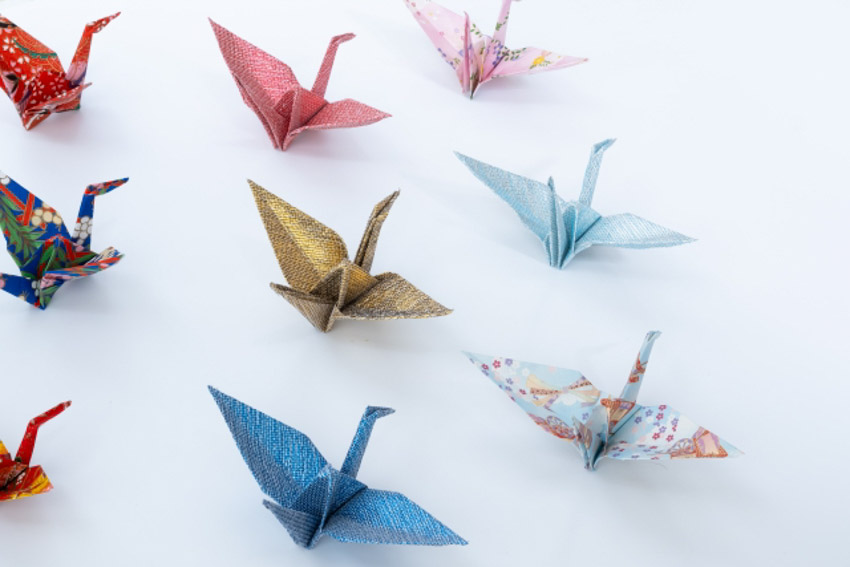 Nine origami cranes in different colors and patterns on a white table