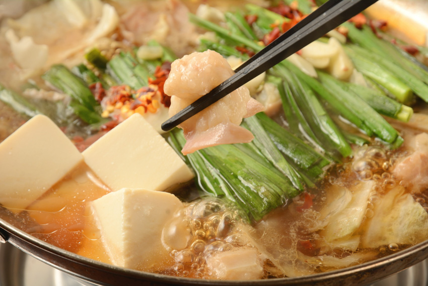 Close up of boiling nabe pot with a pair of chopsticks holding some food