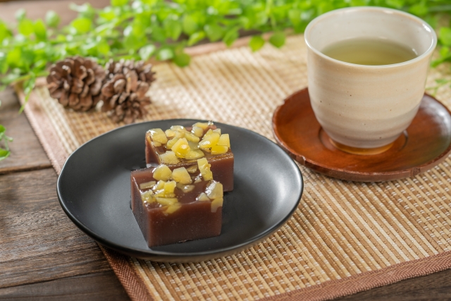 Two pieces of yokan on a black round plate with a cup of green tea next to it