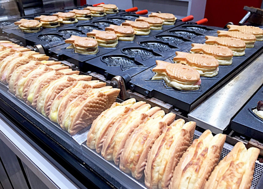 Taiyaki being made on a large taiyaki iron and taiyaki being cooled off on next to the iron