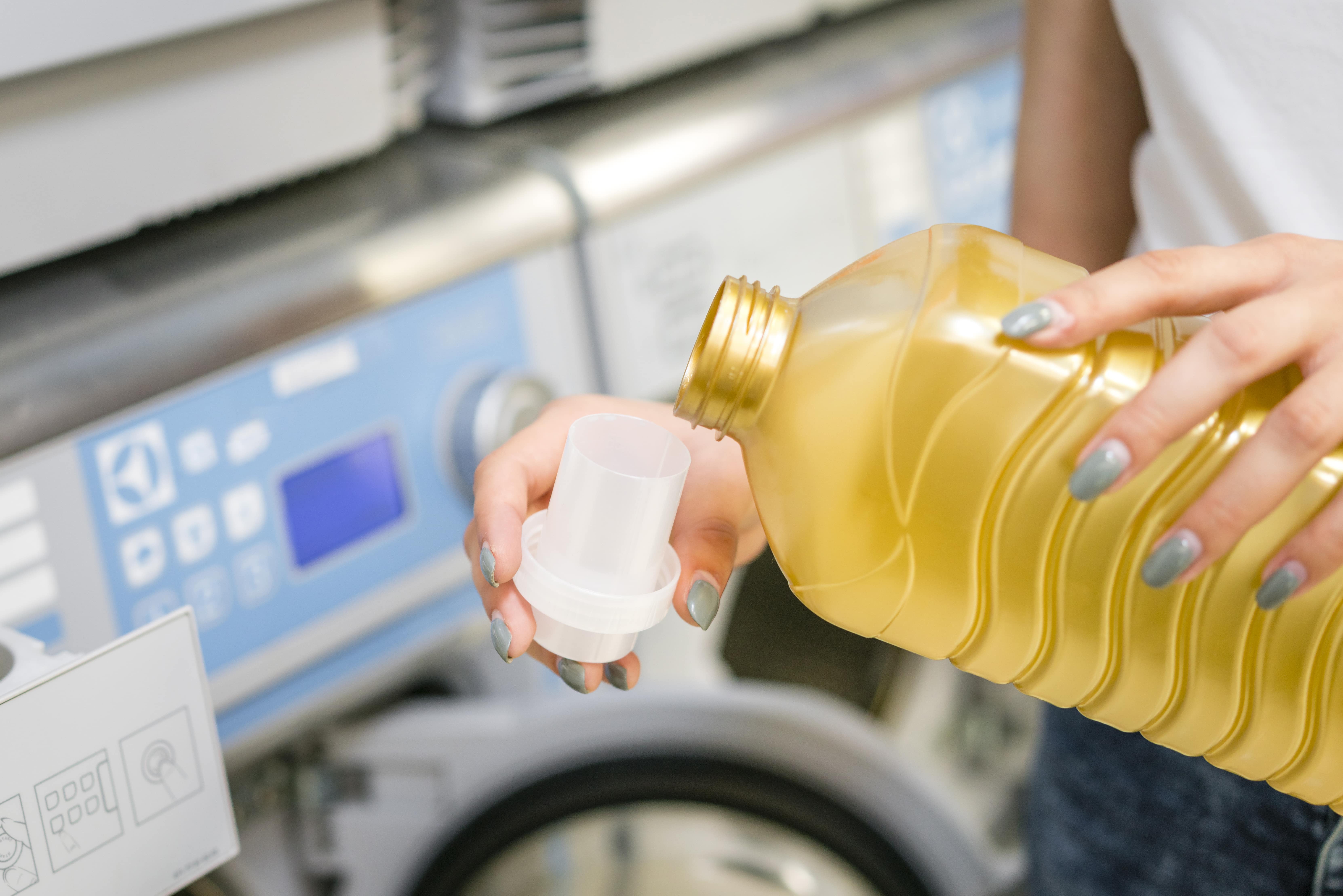 Person pouring laundry detergent into cap with washing machines in the background