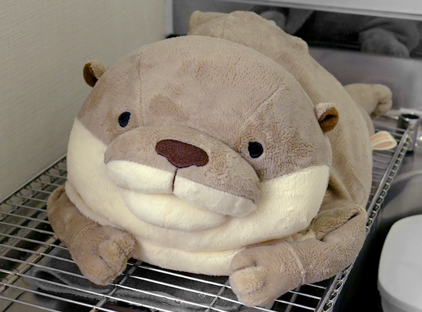 Stuffed gray otter laying on stomach on metal rack in kitchen