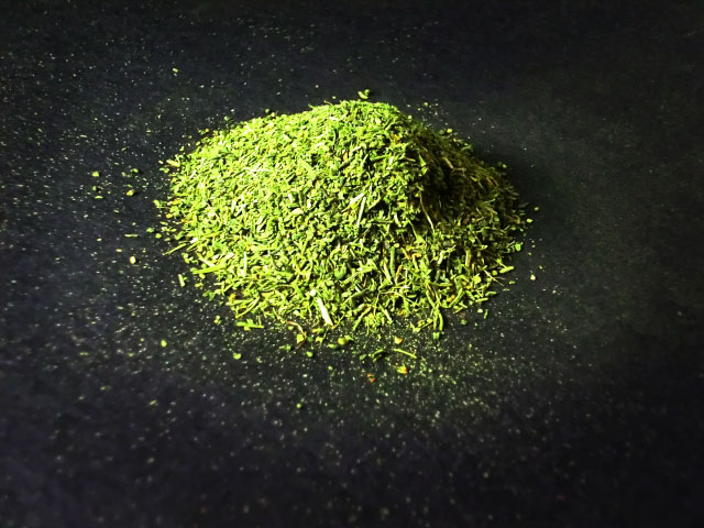 A small pile of bright green dried matcha leaves on a black surface