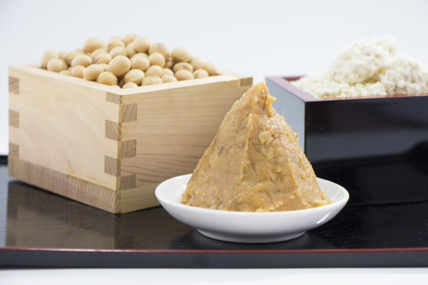 Miso pase on a plate with wooden sake cups behind filled with soybeans and white miso paste