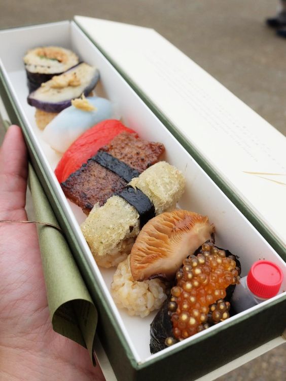 A person holding a box filled with different types of vegan sushi