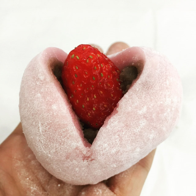 A hand holding a strawberry daifuku with the strawberry sticking out of the top