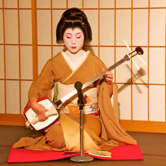 A person dresses as a Maiko playing the Shamisen