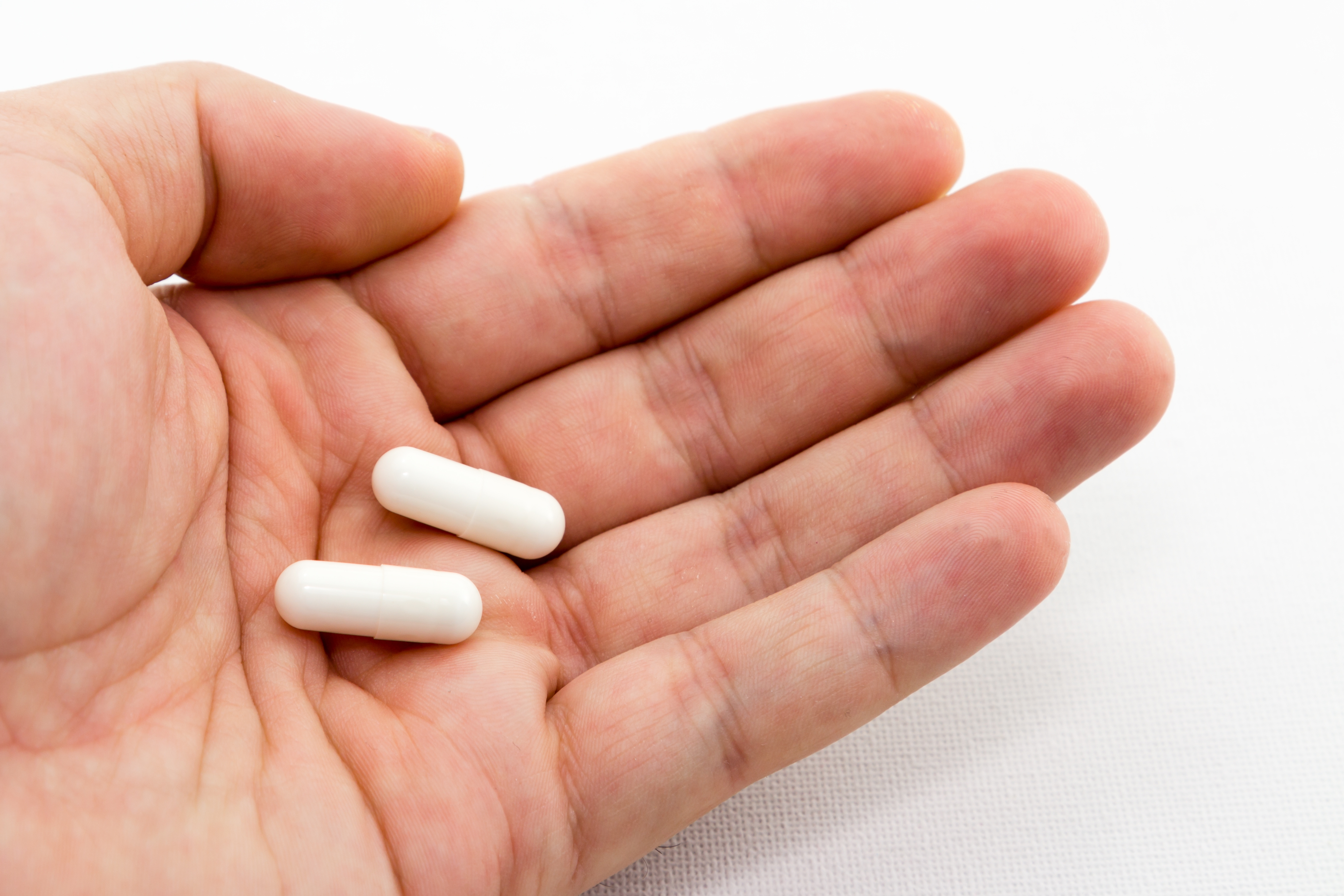 2 long white tablets in person's hand with white background