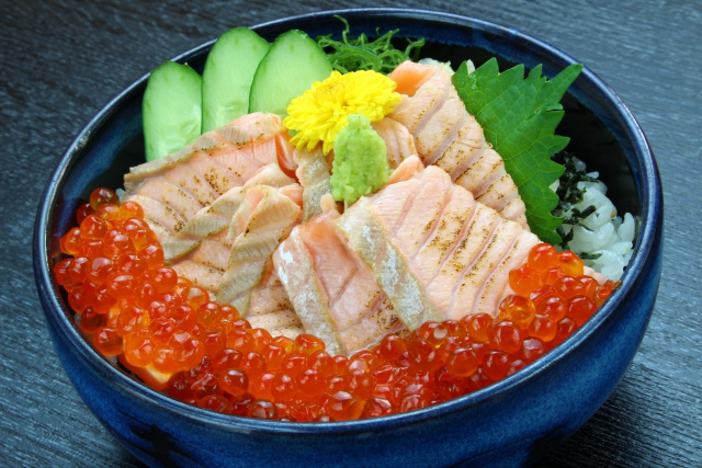 Close up of a bowl of Ikuradon, salmon roe with grilled salmon and some vegetables on top of rice