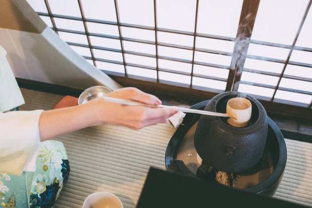 A person using a bamboo server to get hot water from an old style Japanese tea pot