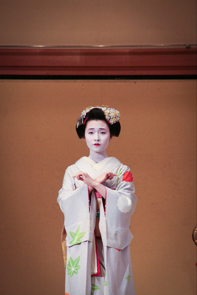 A woman dressed in kimono with flower ornaments in her hair and white face make up 