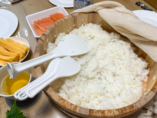 Wooden bucket with cooked white rice inside surrounded by different types of ingredients 