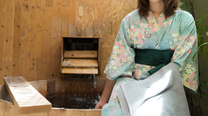 Woman wearing a yukata sitting next to a Japanese hot spring bath