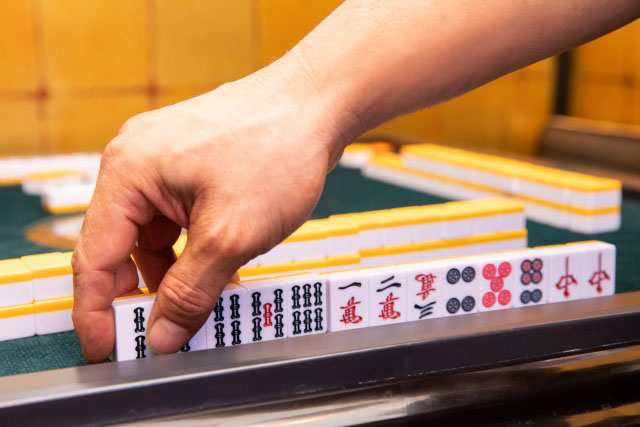 Close up of a hand placing mahjong pieces in a row on a mahjong table