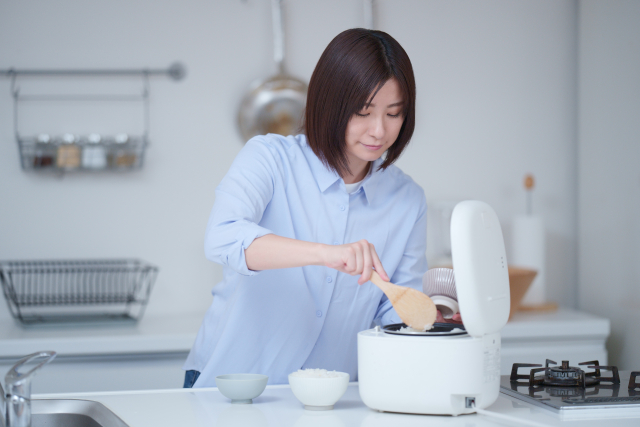 A woman getting herself rice from a rice cooker