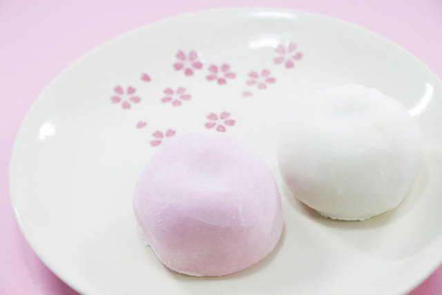 A white and a pink colored daifuku on a small plate decorated with cherry blossoms