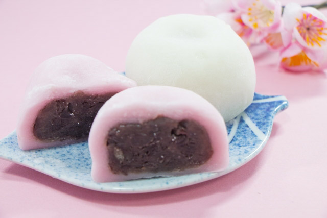 A with daifuku and a pink daifuku with anko inside cut in half on a plage